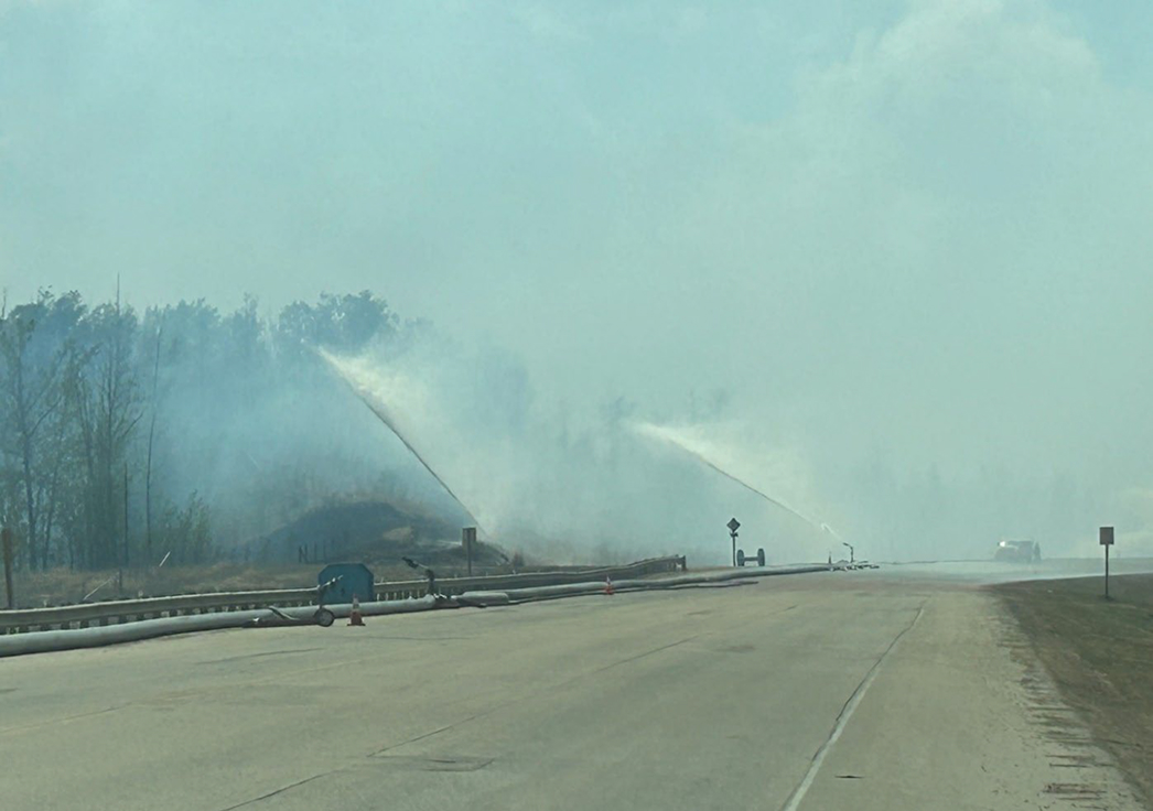 Roadside wildfire with sprinklers spraying water on smoky highway