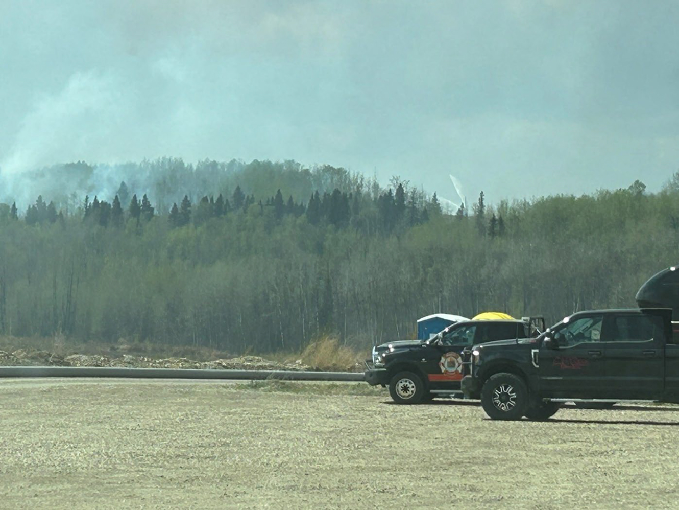 Firefighters battling forest wildfire near parked trucks