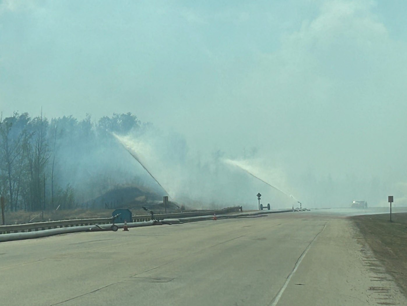Sprinklers spraying water on smoky roadside wildfire