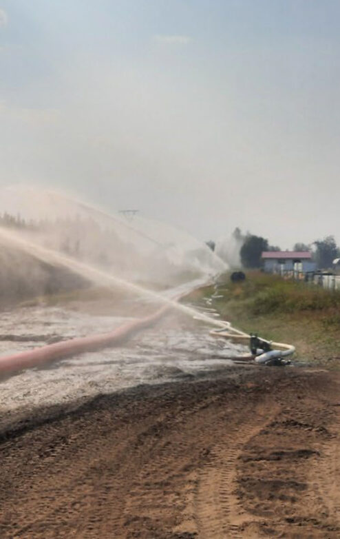 Large hoses spraying water across dirt field