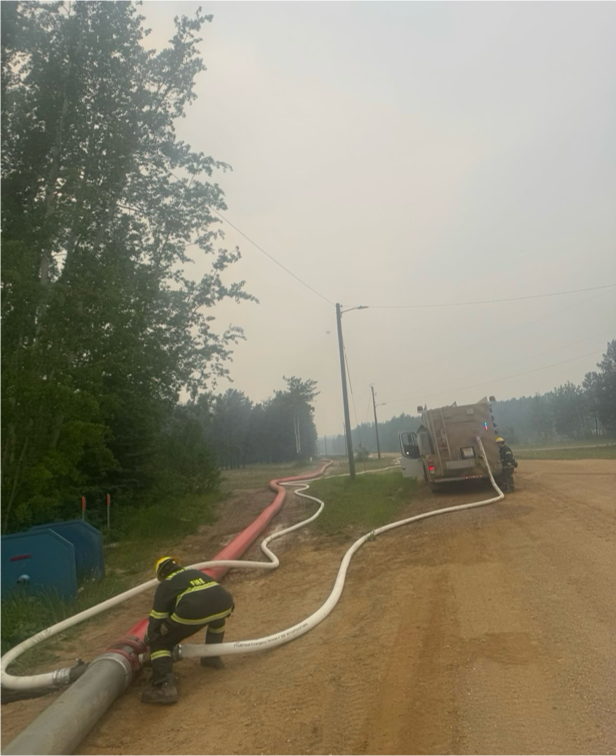 Firefighters connecting hoses to truck on smoky rural road